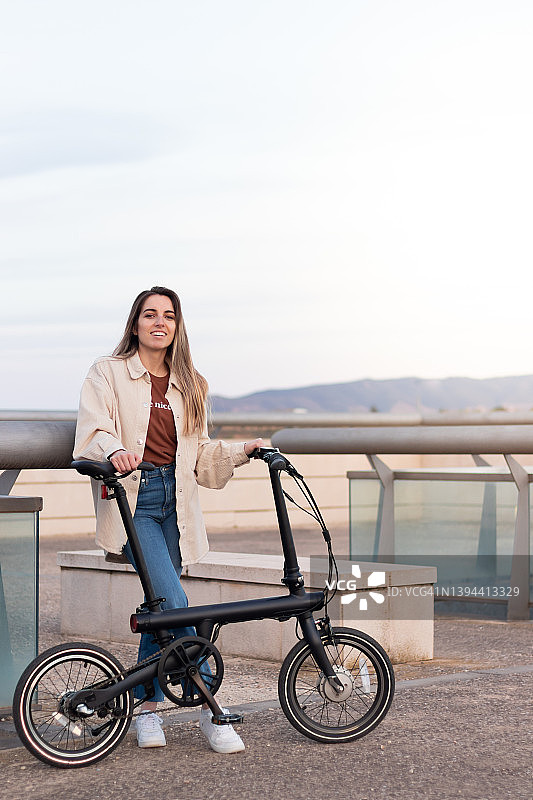 垂直视角的女人幸福和微笑的相机，持有电动自行车在城市的复制空间图片素材