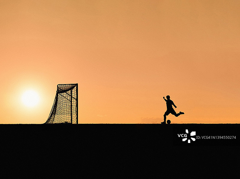 日落时在球场上踢足球的剪影男子图片素材
