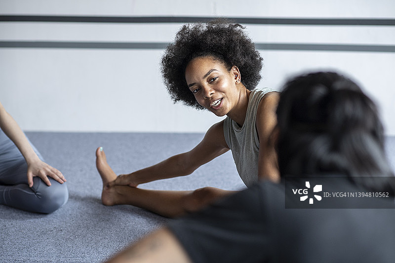 卷发的非洲裔美国妇女在健身课上一边聊天一边伸展身体图片素材