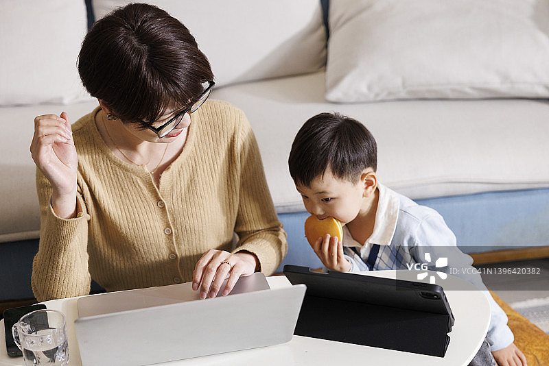 儿子一边吃着面包，一边看着妈妈在电脑前工作图片素材
