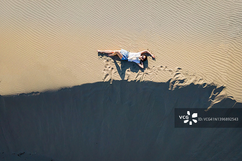女人躺在沙漠景观起伏的沙丘上图片素材