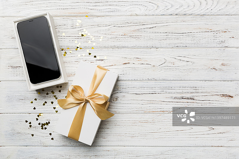 打开礼品盒与金色丝带和智能手机上的彩色背景，俯视图。空白开箱包装模型，模板为您的设计-品牌模型图片素材