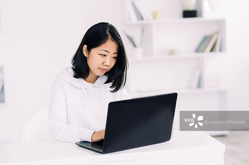 东亚年轻女子在家里使用笔记本电脑工作。远程工作的概念图片素材