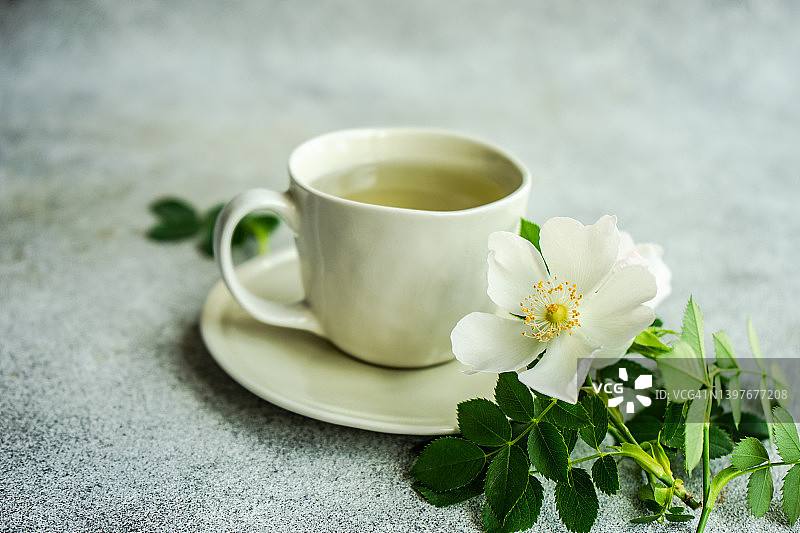 桌上放着一杯绿茶，旁边放着白色的野玫瑰图片素材