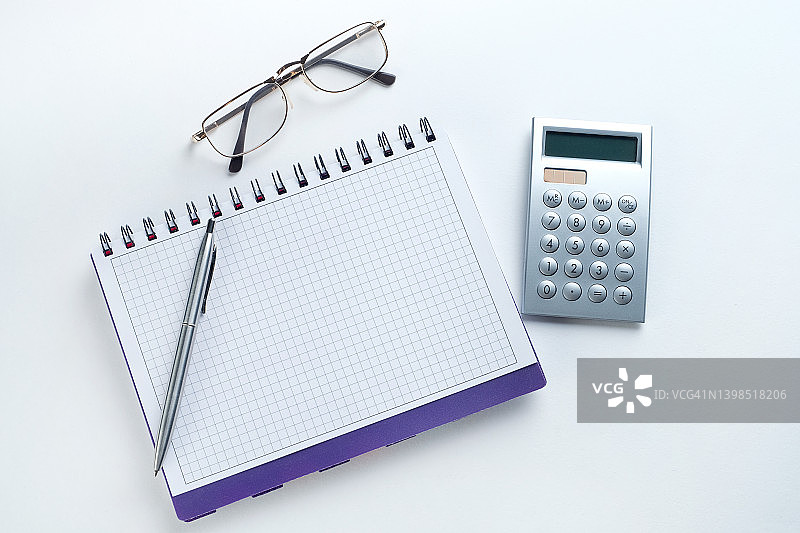 一支笔，一个计算器，一个打开的空白笔记本和一副眼镜。记账簿:商人或会计记录的笔记本财务报表的概念，公司盈亏的计算，费用和收入的管理。图片素材
