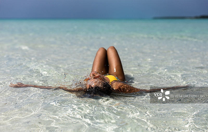 一个女人在沙滩上的浅水中晒日光浴。图片素材