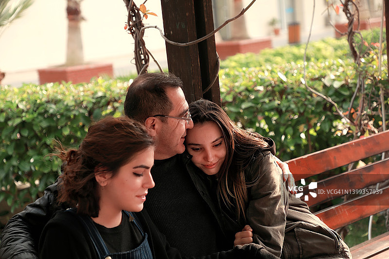 特写肖像的父亲和两个年轻的成年女儿坐在公园的长凳图片素材