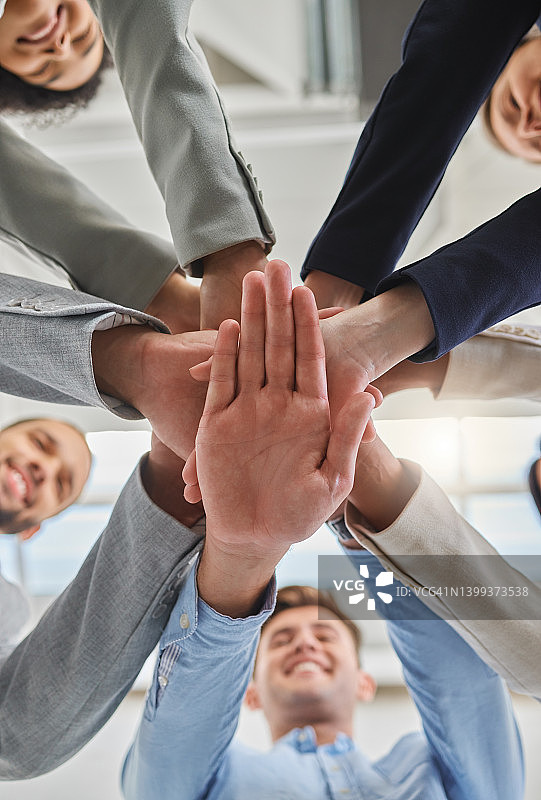一群商务人士在办公室里把手叠在一起工作。商务人士从下面举起双手，享受站着的乐趣图片素材