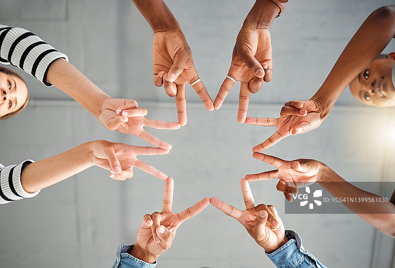 一群商务人士在办公室里用他们的手一起做一个明星形状。商务人士喜欢做手势。同事们在下面做着和平的手势图片素材