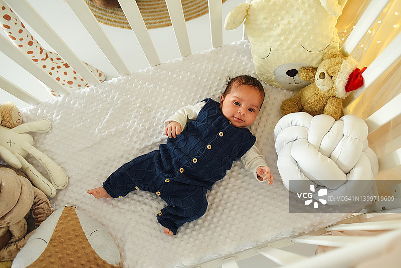 一个黑皮肤的黑白混血婴儿躺在婴儿床上。婴儿穿着蓝色针织连体衣。甜蜜的宝贝。图片素材