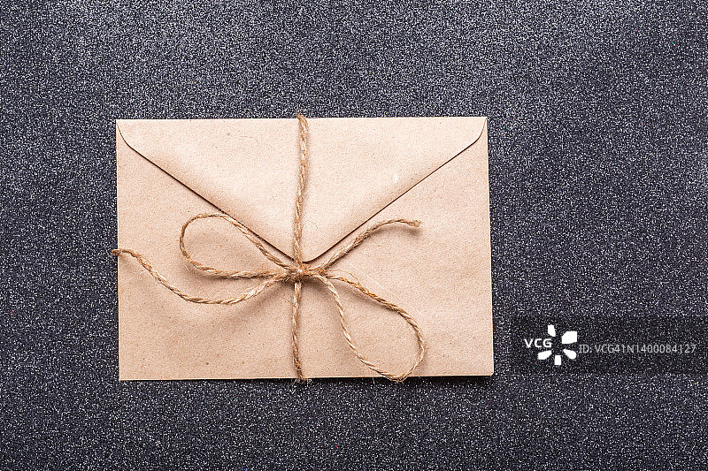 封闭的棕色工艺信封用麻绳与一个蝴蝶结在黑色的背景。一个信封，祝贺你图片素材