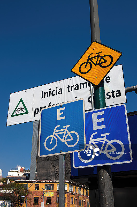 主要城市道路上的各种西班牙语自行车标志，包括一条自行车道、一个自行车停放站，以及一个写着“Inicia tramo de preferencia ciclista”(自行车喜好部分开始)的标志。图片素材