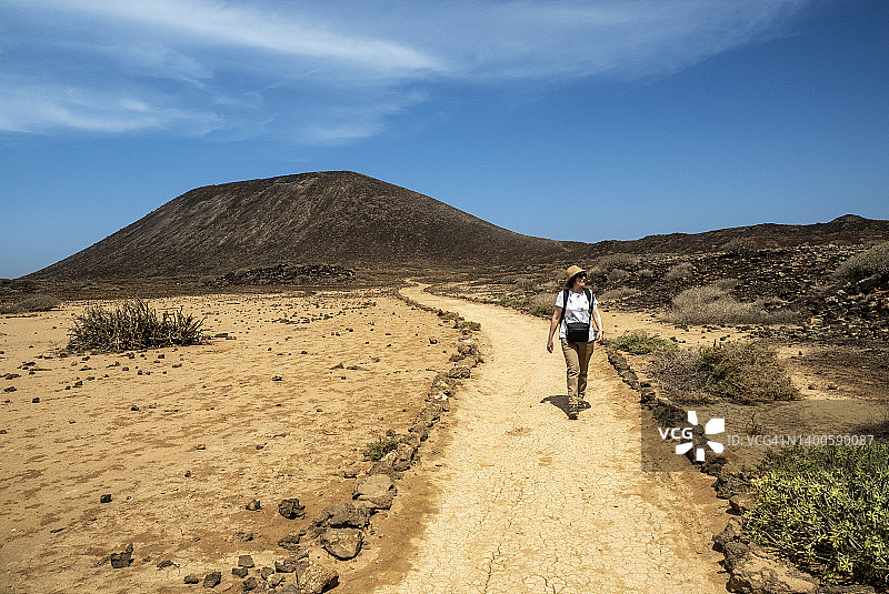 徒步旅行的女人在火山地形的山路上行走。图片素材