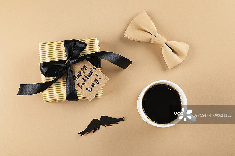 祝您父亲节快乐。咖啡杯，小胡子，蝴蝶领结和礼物盒呈现在米色背景。平铺，俯视图图片素材