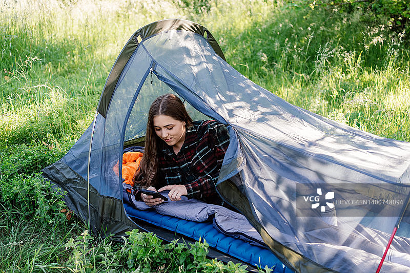 野外的年轻女性在露营时使用手机。图片素材
