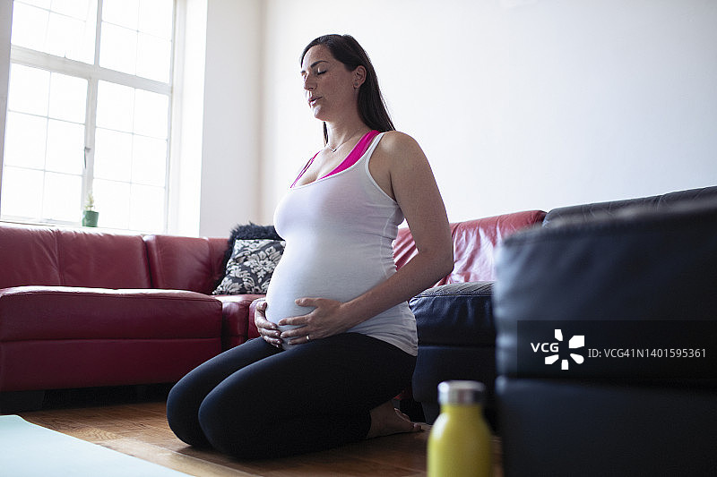 安详的孕妇在客厅地板上做呼吸练习图片素材