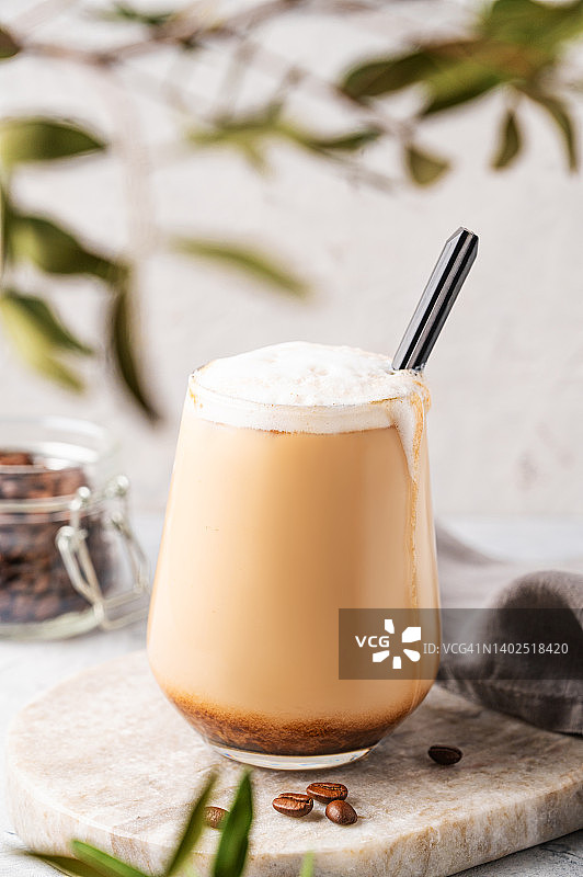 卡布奇诺或拿铁与牛奶泡沫在一个杯子与咖啡豆轻大理石背景与树枝关闭。前视图图片素材