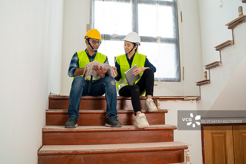 印度男工人和亚洲女工程师或经理在建筑工地的楼梯上一起工作图片素材