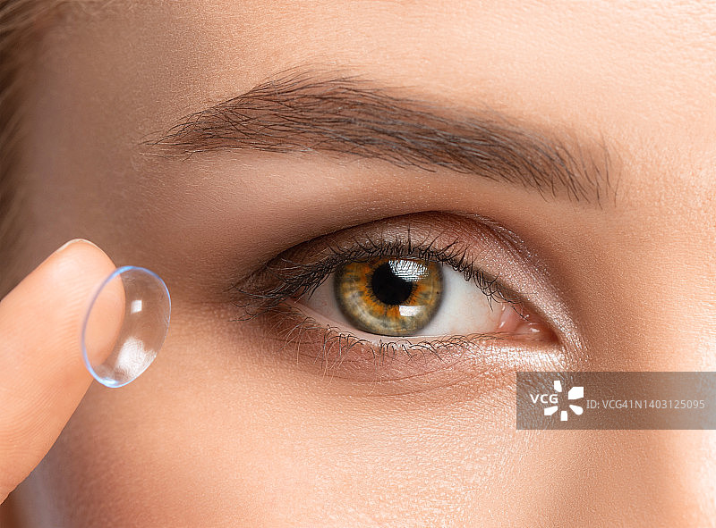 美女把隐形眼镜戴在手指上。眼睛护理和改善视力的手段之间的选择。图片素材