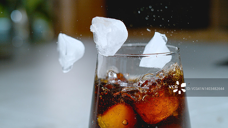 特写:冰块掉进玻璃杯后，黑色的苏打水飞溅开来。图片素材