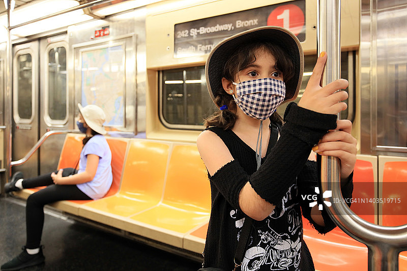 两个年轻女孩戴着防护口罩乘坐纽约地铁。图片素材