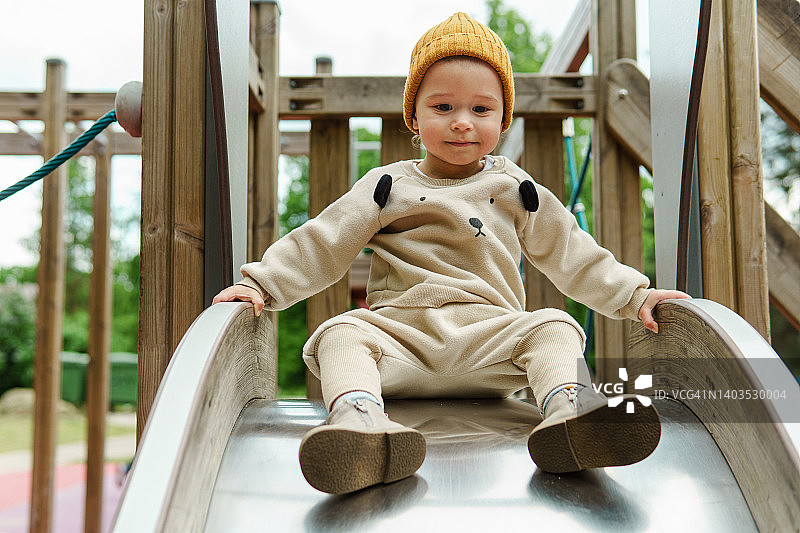 可爱的小男孩坐在公园里的滑梯上图片素材