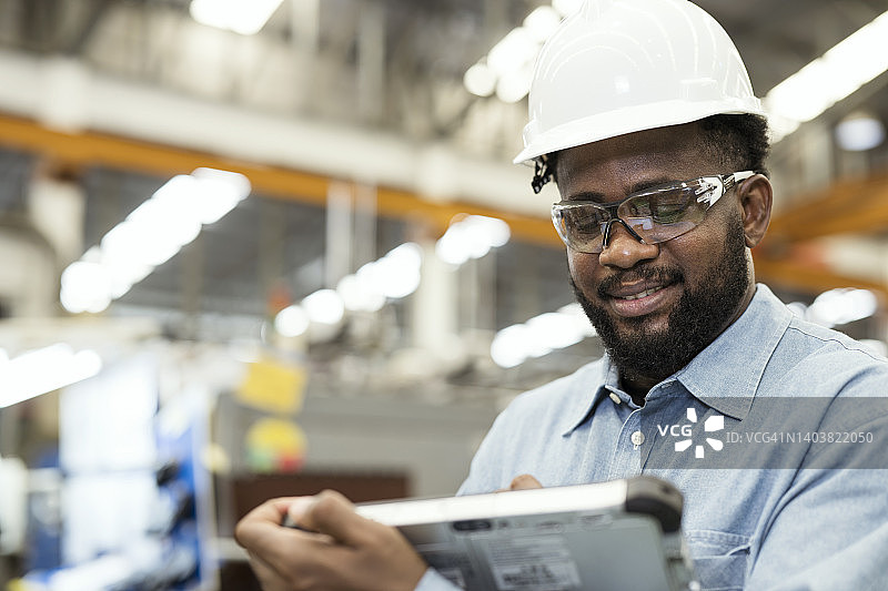 注塑行业的生产运营管理。一名男性非洲裔美国人在塑料工程零件行业工作，同时使用平板电脑管理注塑工艺的工作流程。图片素材
