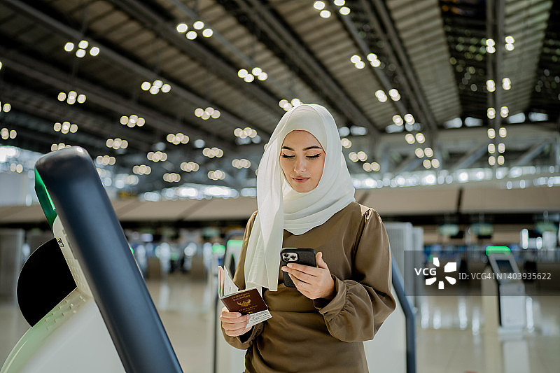 亚洲穆斯林妇女在机场使用登机机领取登机牌。图片素材