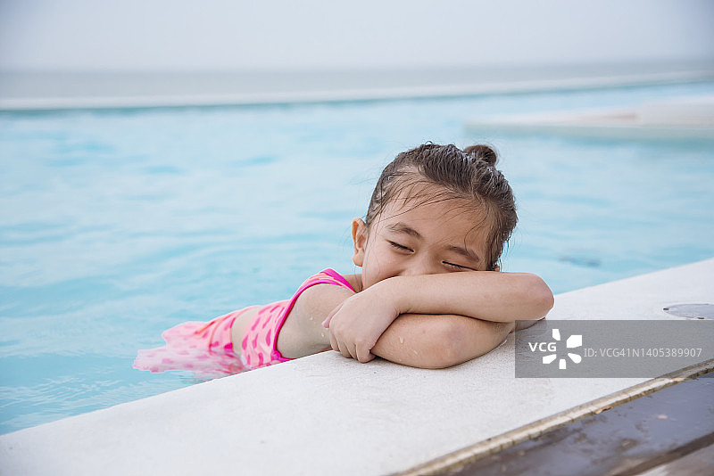 蹒跚学步的女孩有乐趣的游泳池夏季时间与泳装在蓝色的水在酒店游泳池室外。孩子们在暑假里游着好玩的水花。快乐女孩游泳概念图片素材
