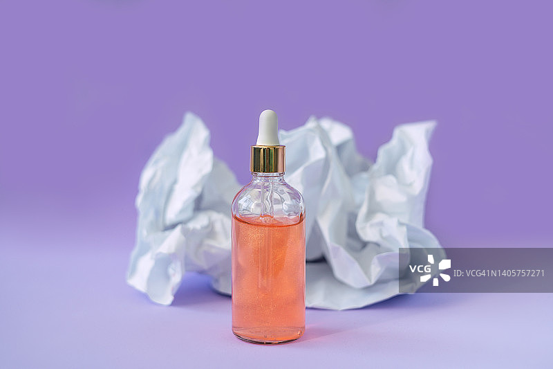 紫色背景的带吸管的面部血清玻璃瓶。图片素材