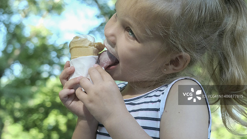 可爱的小女孩在外面吃冰淇淋。特写的金发女孩坐在公园的长凳上吃冰淇淋。图片素材