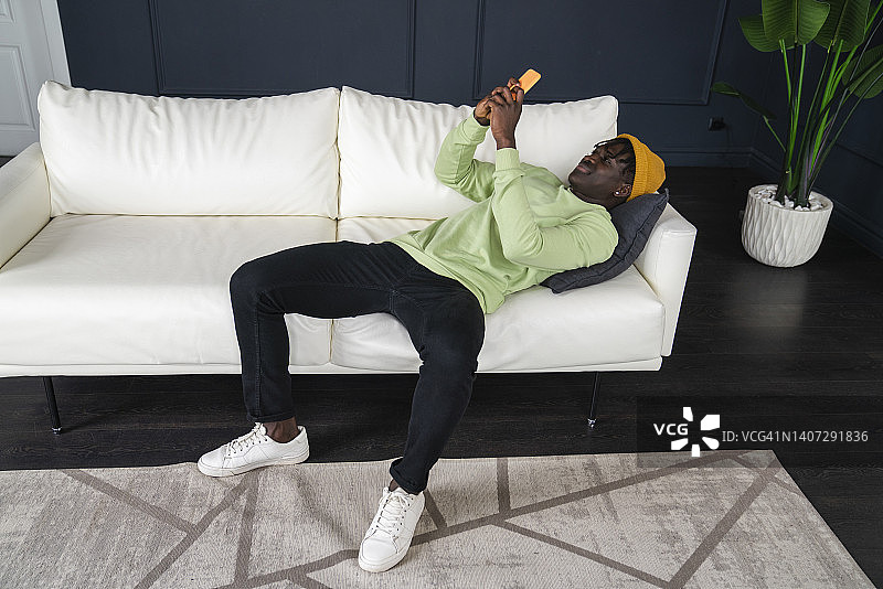 年轻人躺在家里的沙发上用智能手机图片素材