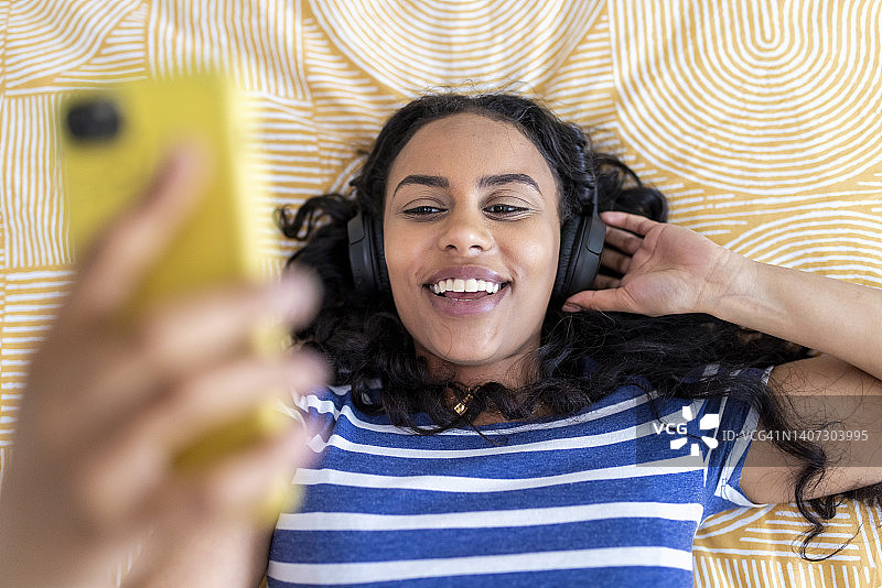 快乐的女人在卧室里戴着耳机和智能手机图片素材