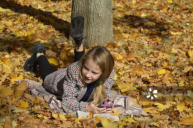 女孩躺在公园的落叶上看书图片素材