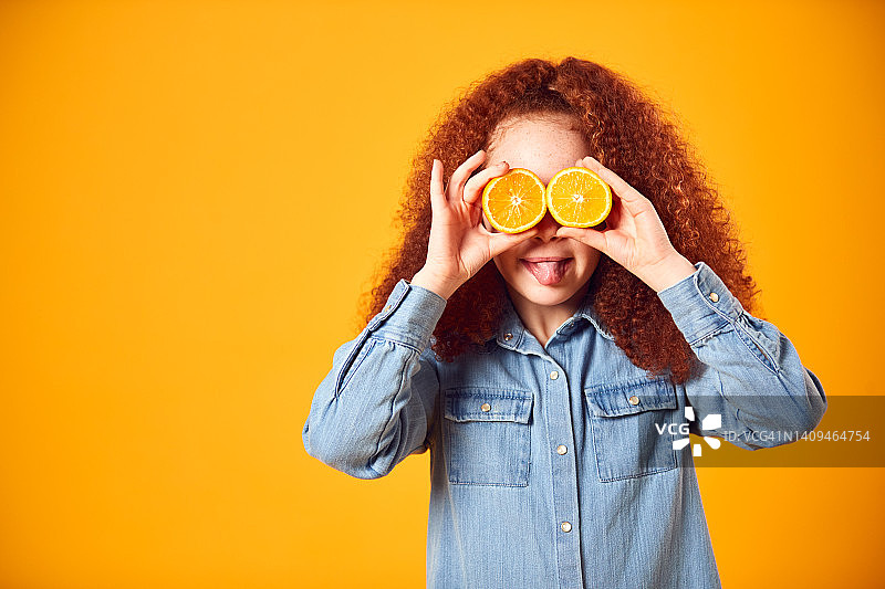 工作室肖像的女孩拿着两个橙色的一半在前面的眼睛对黄色的背景图片素材