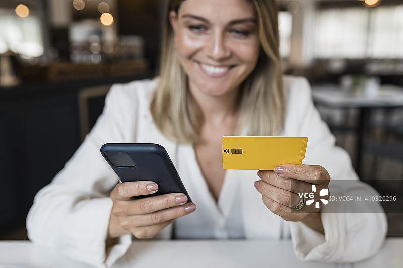 微笑的女商人拿着信用卡在餐厅通过智能手机网购图片素材