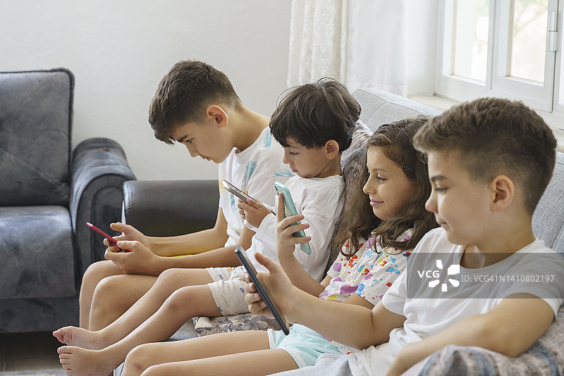 一群孩子在家里坐成一排玩手机图片素材