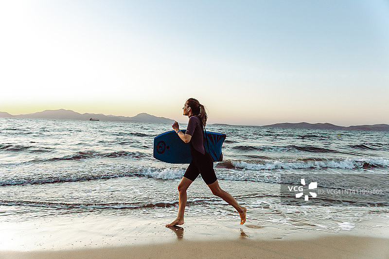 一个年轻女人的剪影在沙滩上跑步，手里拿着冲浪板图片素材