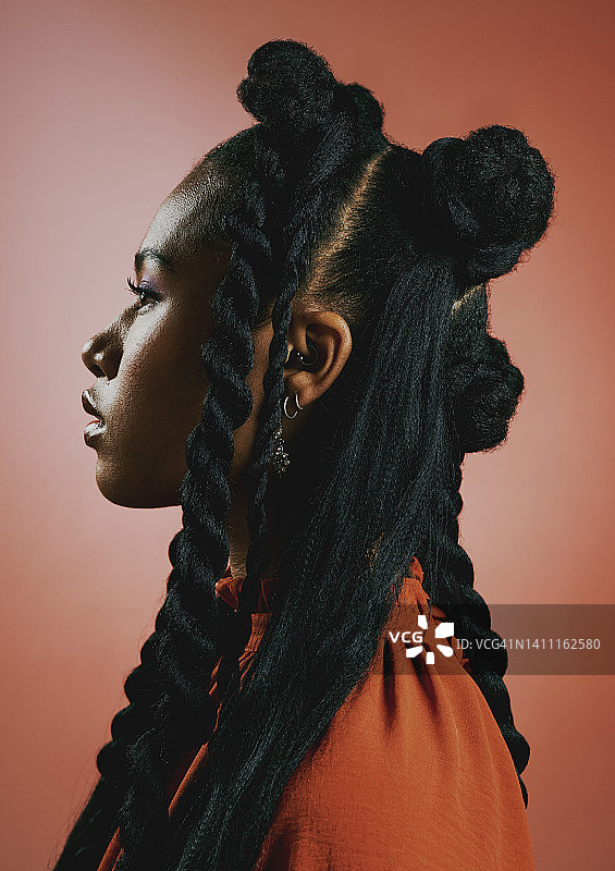 前卫的年轻黑人女性，梳着时髦的麻花辫发型，映衬着橙色的画室背景。一个自信，严肃和时尚的非裔美国女性的侧面，大胆的个性和冷静的态度图片素材
