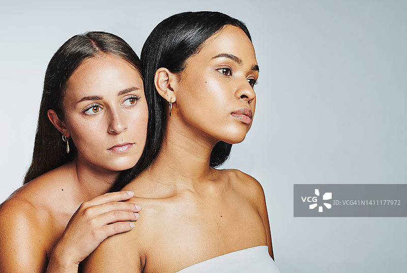 两个完美的女人与发光的皮肤孤立在演播室背景。多元文化的美丽模特的脸看起来自信和授权，他们的自然，清洁和保湿的皮肤护理程序图片素材