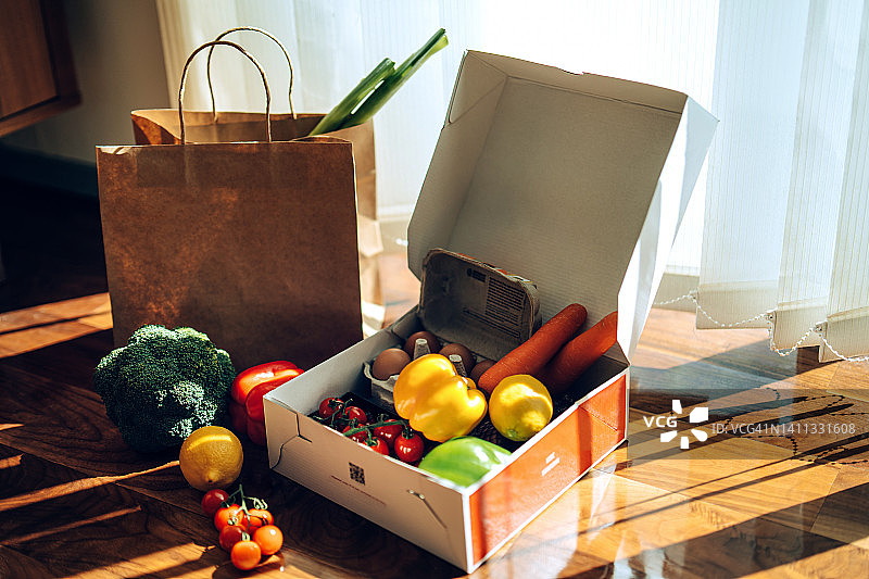 在阳光下的木制背景下，一个装满了五颜六色的新鲜有机水果、蔬菜和杂货的送货纸箱。杂货店订阅框。餐包。日常生活方便，节省时间图片素材