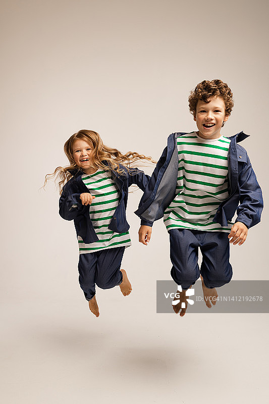 一个男孩和一个女孩穿着牛仔裤和衬衫，在画室的白色背景上的肖像，在快乐，跳跃，笑图片素材