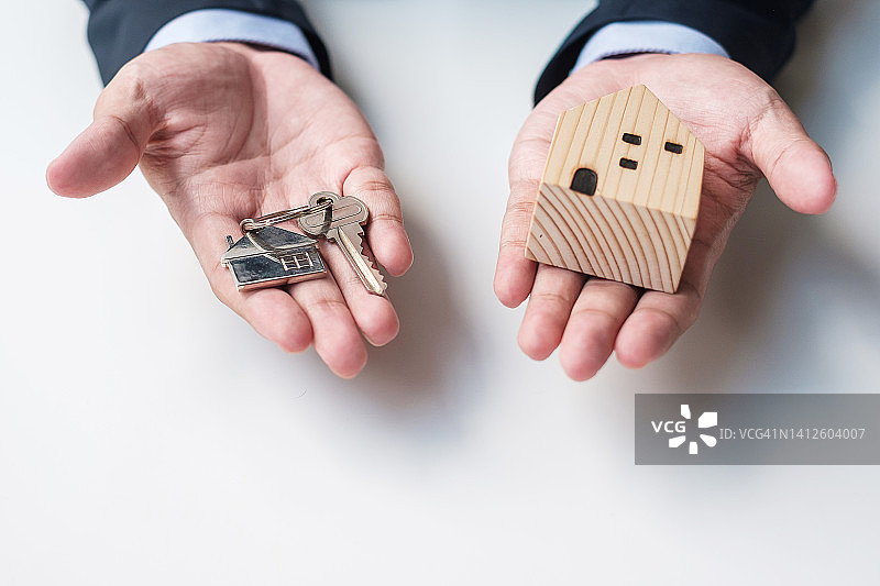 商人手握钥匙与木制家居模型。房地产买卖、财产保险、租赁及合同协议的概念图片素材