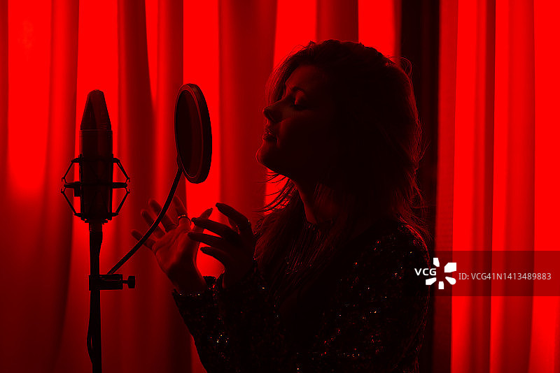 剪影女歌手唱歌和录音歌曲的录音棚在红色发光的背景图片素材
