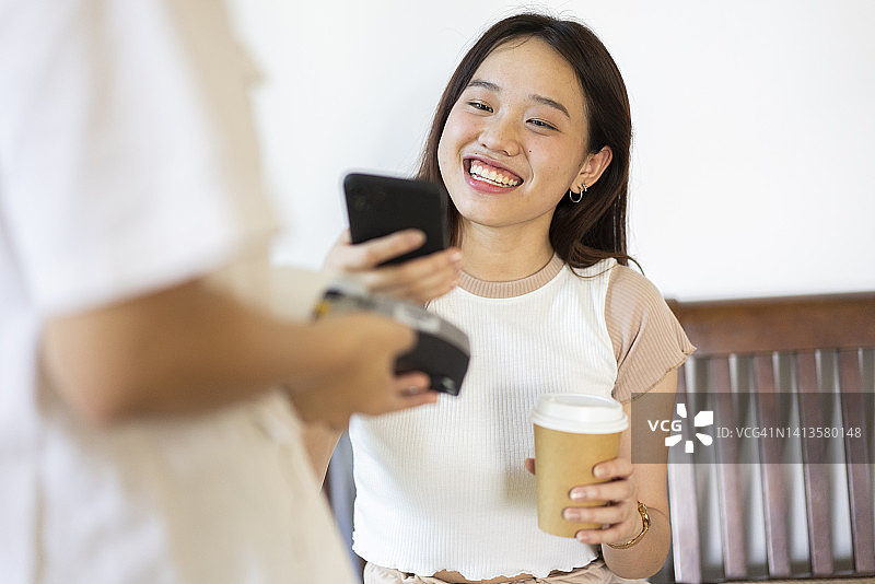 积极情绪亚洲青少年Z世代使用智能手机扫描和交易非接触式支付购买外卖咖啡图片素材
