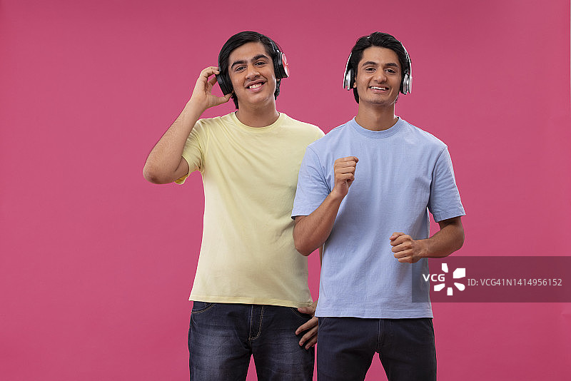 两个快乐的朋友在粉红色的背景下听音乐图片素材