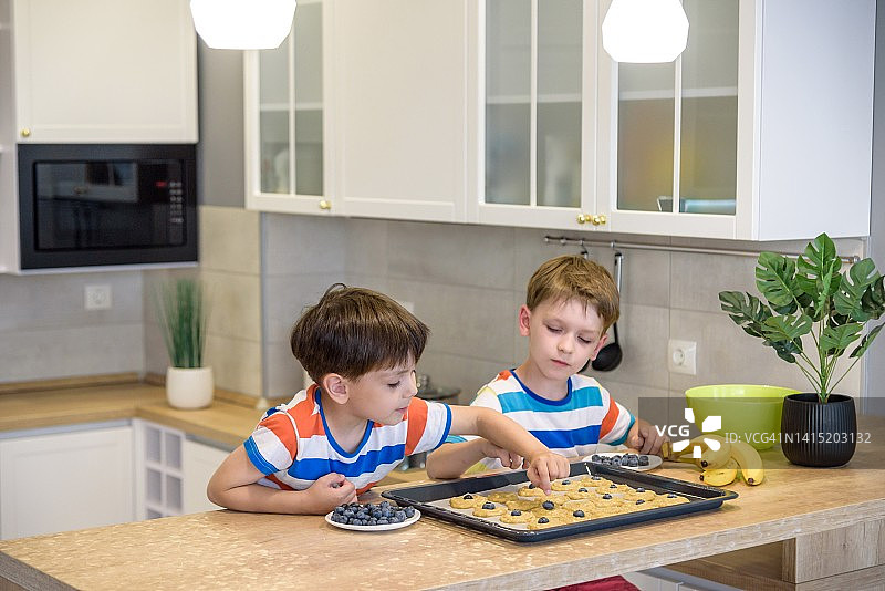 快乐的家庭有趣的孩子们正在厨房准备面团，烤饼干。把浆果和蓝莓放进所有的饼干里图片素材
