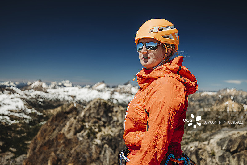 一位身穿橙色夹克的女子站在一座风景优美的山顶上图片素材