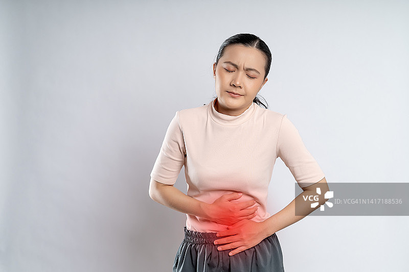 一名亚洲妇女胃痛，把她的手放在肚子上有红斑。图片素材