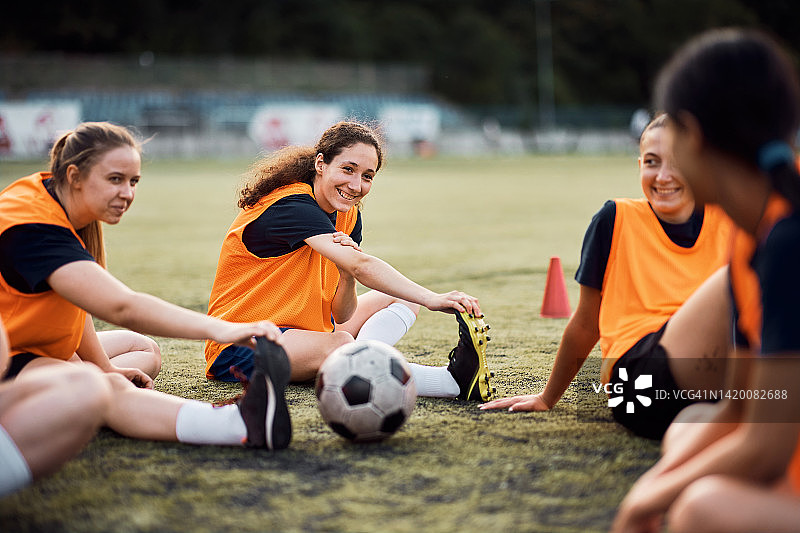 快乐的女子足球队在运动训练场上伸展腿。图片素材
